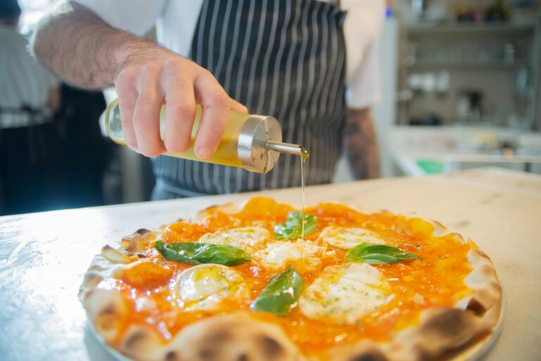 Chef drizzling olive oil on fresh Margherita pizza in a restaurant kitchen.